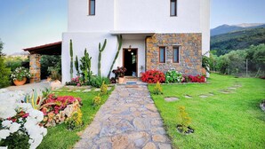 A modern two-story house with a stone facade, a stone pathway leading to the entrance, and a well-maintained garden with various plants and flowers. - Private Pool & Garden Villa for 6 (Pemonia)
