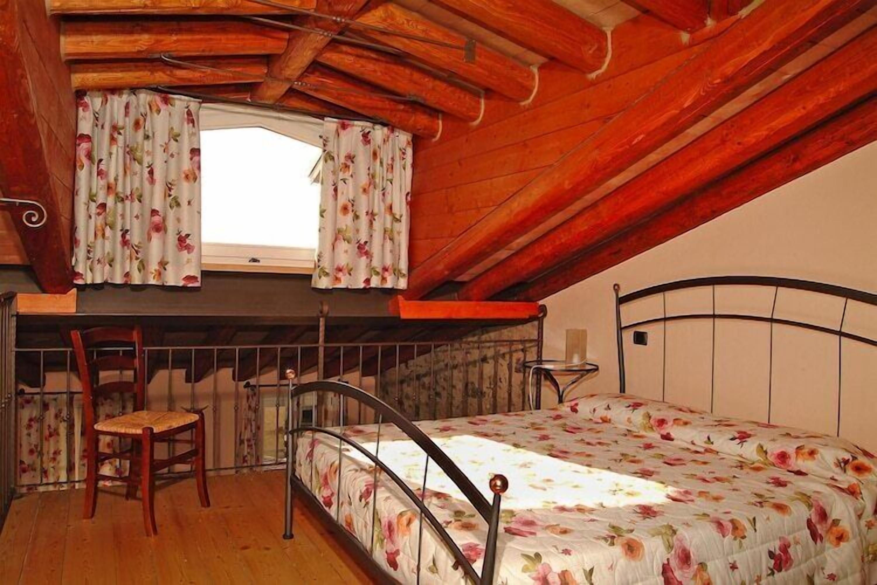A small, rustic attic bedroom with a single bed, a wooden chair, and a window with floral curtains.