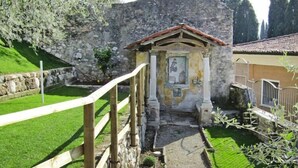 Une petite chapelle rustique, dotée d’un mur en pierre et d’un toit en tuiles, entourée d’une clôture en bois et d’une pelouse bien entretenue.
