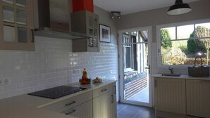 Moderni keittiö, jossa on valkoiset metrotyyliset seinälaatat, musta induktioliesi ja suuri ikkuna, josta avautuu näkymä ulos.