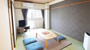 A room with tatami mats, a low table, cushions, a television, and an air conditioning unit.