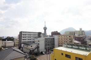 A cityscape with a prominent tower, various buildings, and a mountain in the background. - Guesthouse BJ STYLES (Beppu)