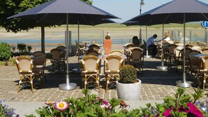 Outdoor seating with wicker chairs and umbrellas, a potted plant, and a view of the beach. - Beachside Flat with Sunny Patio (Cayeux-sur-Mer)