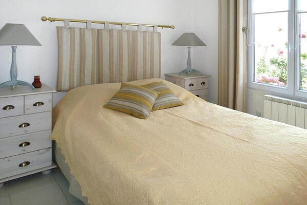 A bedroom with a bed, two bedside tables, a window, and curtains.