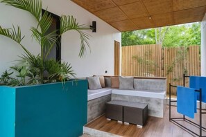 A modern outdoor seating area with a sectional sofa, a small table, and a blue folding chair. - Bird of Paradise (Panglao)