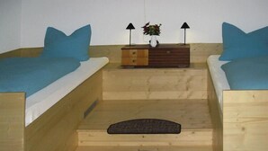 Ein kleiner, gemütlicher Raum mit zwei Holzbett, einem Nachttisch mit Lampe und einem Tisch mit Blumenvase.