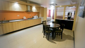 Een kleine keuken met houten kastjes, een magnetron, en een eethoek met een tafel en stoelen.