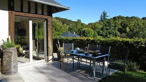 Un espace patio aménagé avec une table et des chaises, un pot de fleurs et une vue sur une colline boisée.