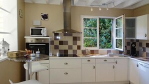 Une cuisine compacte avec des meubles blancs, un four à micro-ondes, une cuisinière et une fenêtre donnant sur un espace verdoyant.