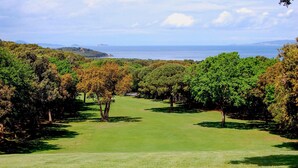Campo de golf con vista despejada al mar y colinas distantes.
