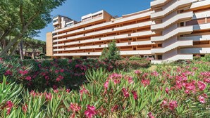 Un hotel de varios pisos con balcones y un jardín lleno de flores rosadas.