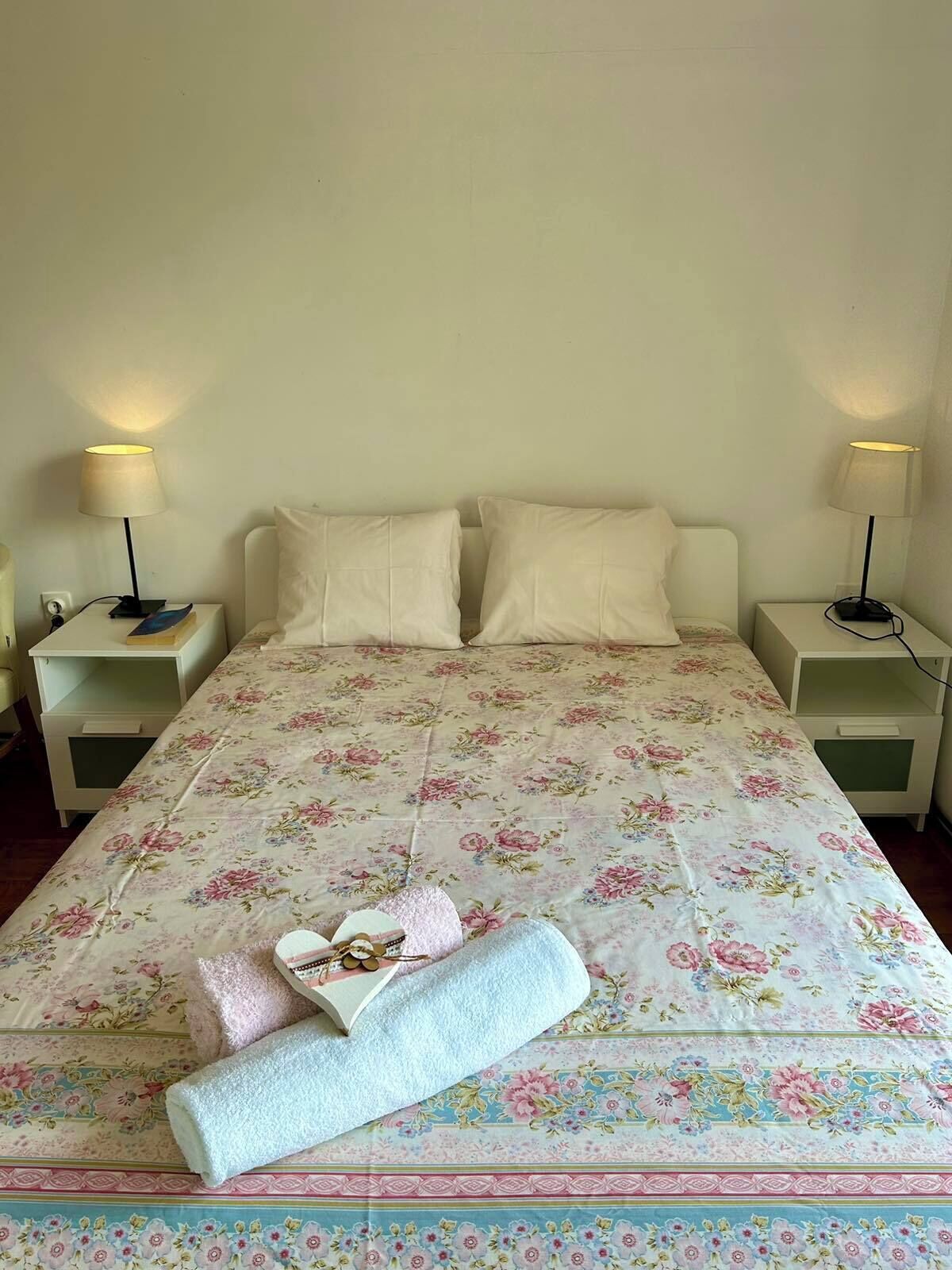 A neatly made bed with a floral bedspread, two pillows, and a rolled towel on the bed.
