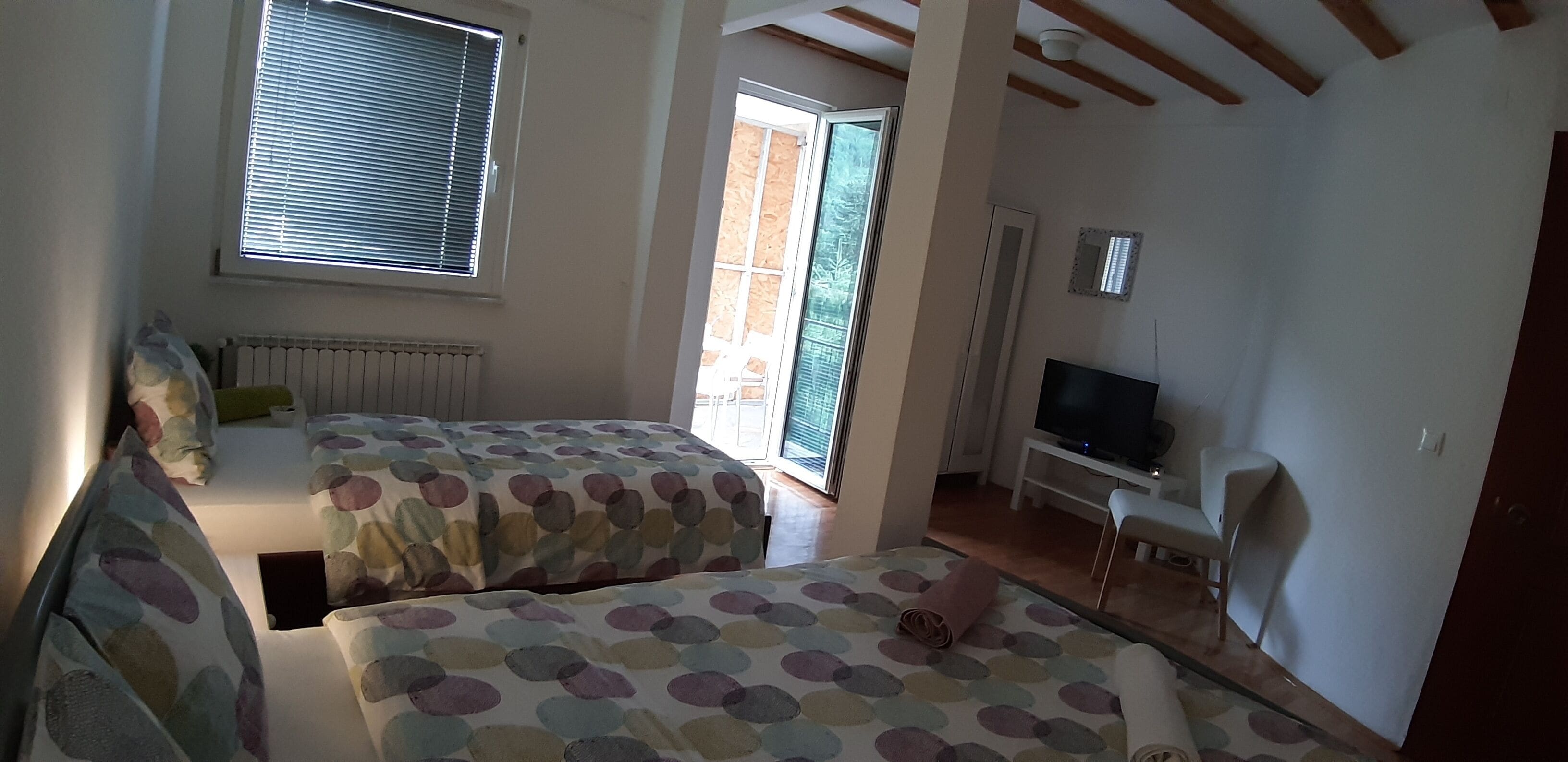 Una habitación con dos camas, televisión y una puerta corrediza de vidrio que da a un espacio exterior.