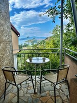 Balcón con una mesa y dos sillas, con vistas a un paisaje pintoresco con árboles y una masa de agua distante.