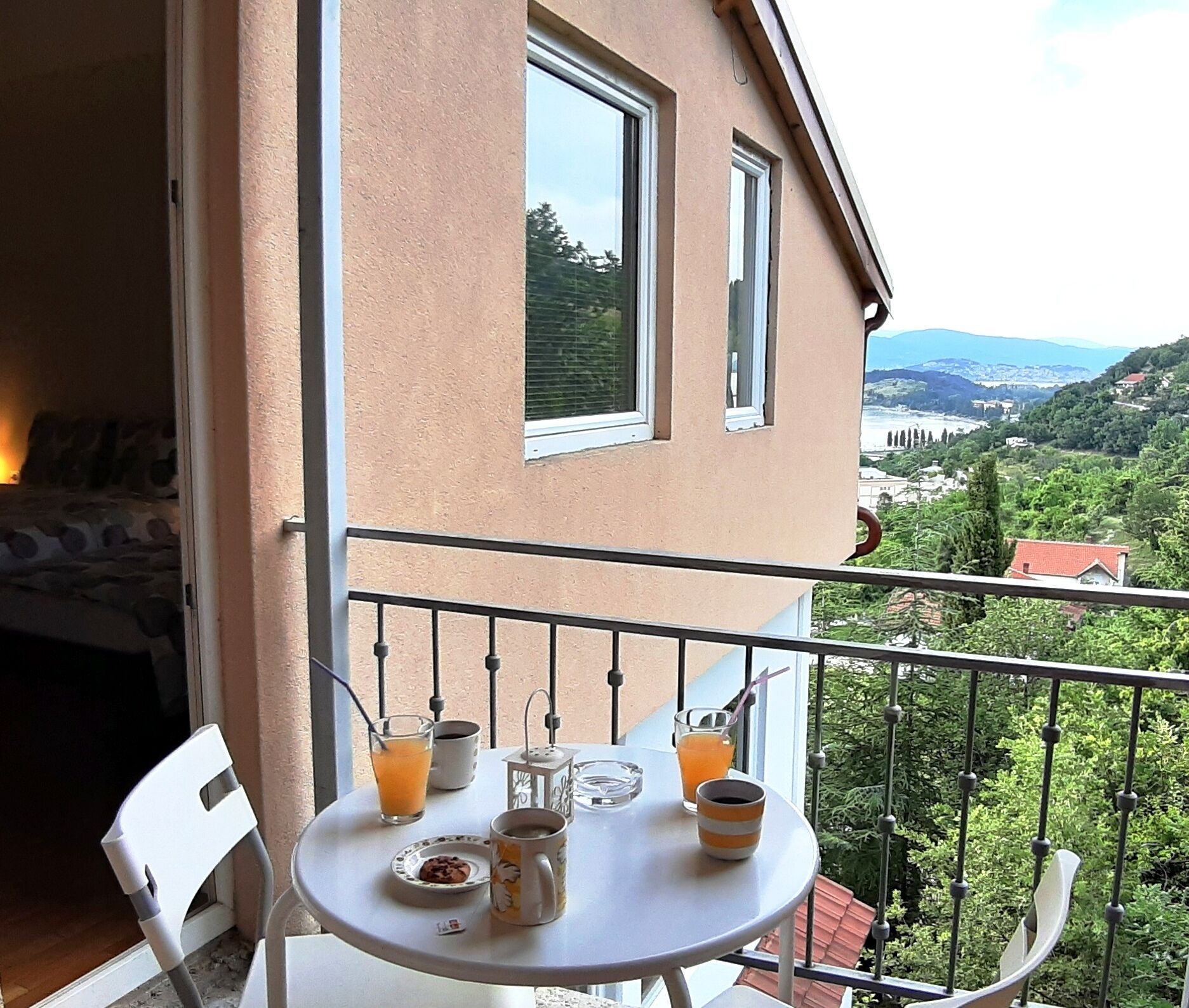 A balcony with a table set for breakfast, including a plate of cookies, a mug, and glasses of orange juice.
