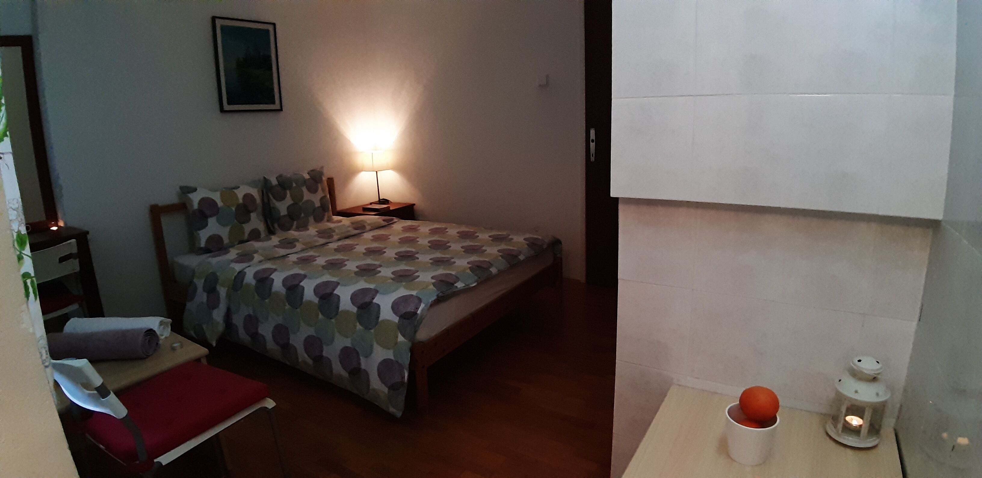 A bedroom with a bed, a nightstand, a lamp, a small table with a cup and a lantern, and a red chair.