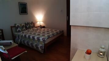A bedroom with a bed, a nightstand, a lamp, a small table with a cup and a lantern, and a red chair.