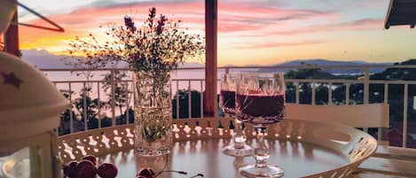 A table with two glasses of red wine, a vase with flowers, and a tray with cherries.