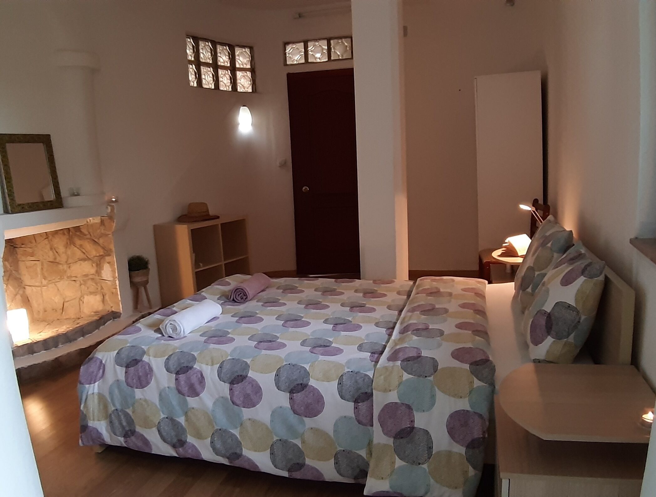 Een slaapkamer met een bed, nachtkastje, kast en een klein raam.