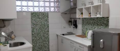Una cocina con armarios blancos, un fregadero, una ventana con entramado y un refrigerador.