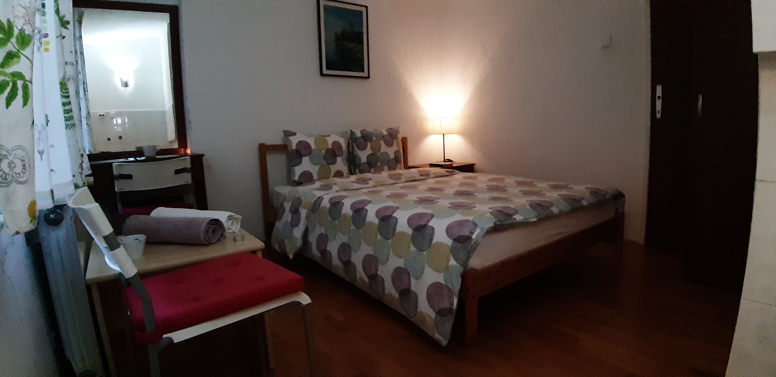 Een slaapkamer met een bed, nachtkastje, stoel, bureau en lamp.