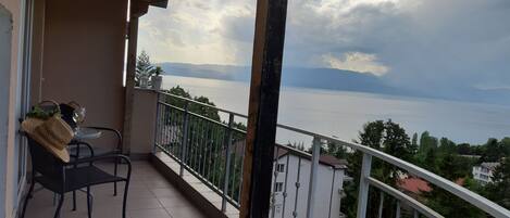 A balcony with a view of a lake and mountains, a table with a chair, and a potted plant.