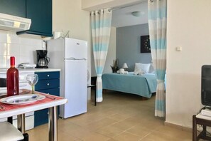 A compact kitchen with a refrigerator, coffee maker, and a dining table set with a wine bottle and glasses.
