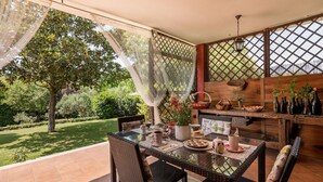 Un patio con tavolo in vetro, sedie in vimini e vista su un giardino.