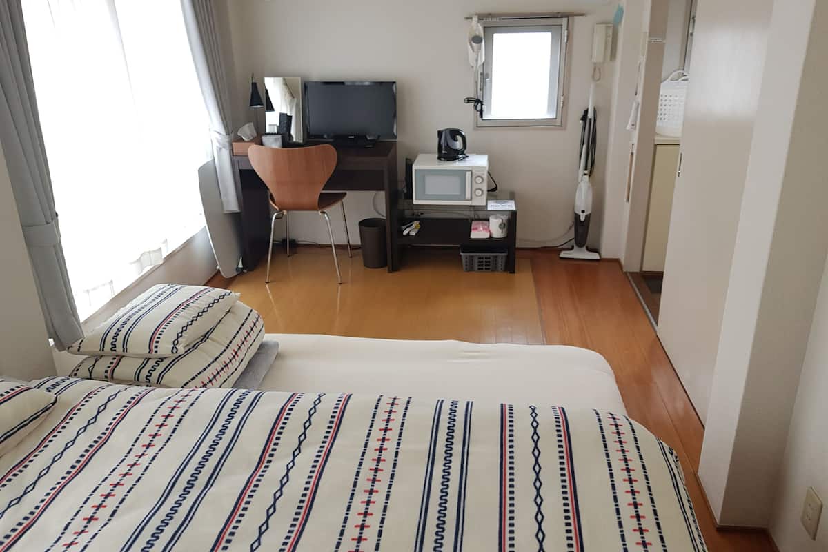 Une chambre d’hôtel avec un lit, un bureau avec un ordinateur, une chaise, un four à micro-ondes et une fenêtre.