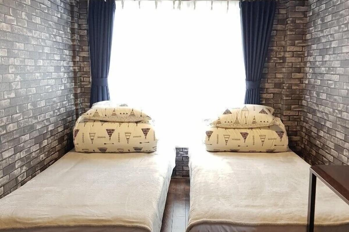 Une chambre avec deux lits, un mur en briques, une fenêtre avec des rideaux et un appareil de climatisation.