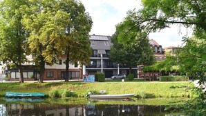 A riverside view with a boat, trees, and buildings in the background. - Appartements mit Blick auf die Spree in Lübben (Lübben)