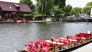 A boat with red upholstered chairs and tables, docked at a canal with a building in the background. - Appartements mit Blick auf die Spree in Lübben (Lübben)