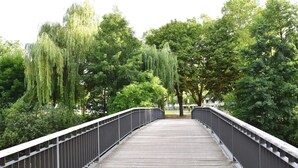 A wooden pedestrian bridge with metal railings, surrounded by lush green trees and a clear sky. - Appartements mit Blick auf die Spree in Lübben (Lübben)