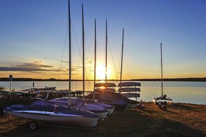 Un port de plaisance où sont amarrés plusieurs voiliers, un ciel dégagé et le soleil qui se couche à l’horizon.