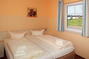 Een tweepersoonsbed met witte lakens, een nachtkastje, een raam met gordijnen en een schilderij aan de muur.