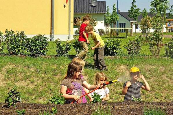 Children gardening in a grassy area with a building in the background.