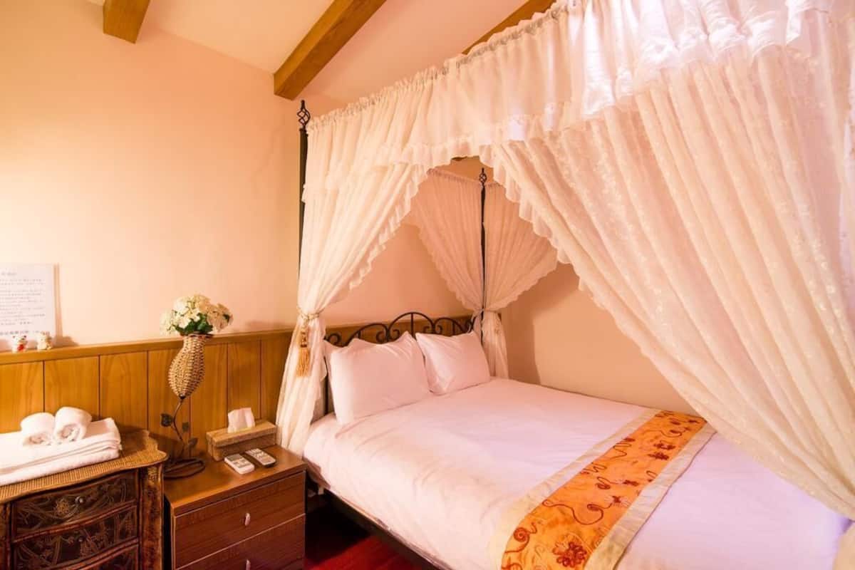 A bedroom with a four-poster bed, a bedside table with a lamp, and a vase of flowers.
