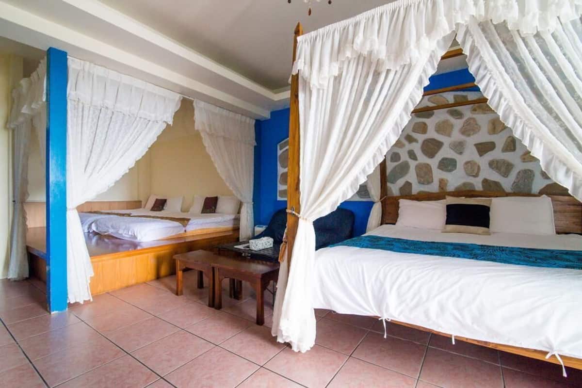 A room with a four-poster bed, two smaller beds, a wooden bench, and a stone-patterned headboard.