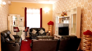 A living room with a red carpet, leather sofas, a TV, and a cabinet with glass doors. - Fantasy Village Hotel (Dodoma)