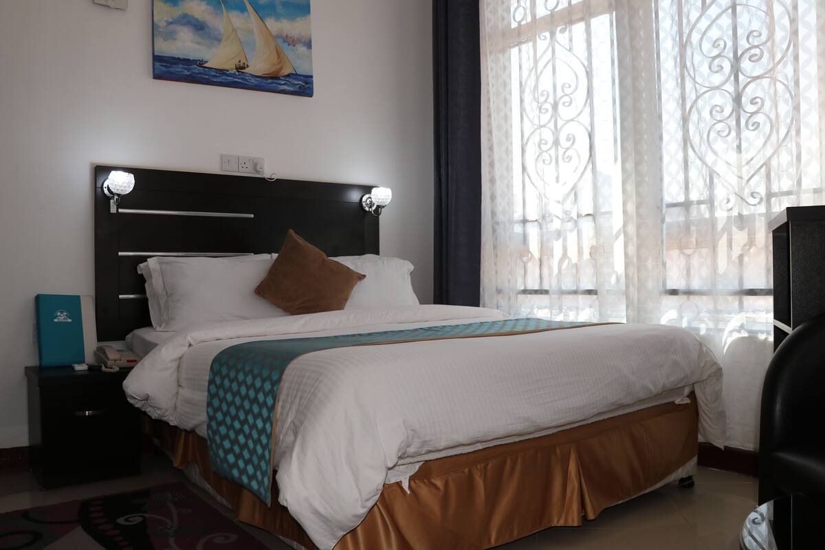 Uma cama bem arrumada com cabeceira, mesa de cabeceira com abajur e um quadro na parede.