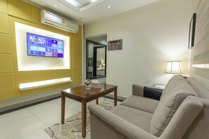 Ein modernes Wohnzimmer mit Flachbildfernseher, einer Couch, einem Couchtisch und einer Lampe.