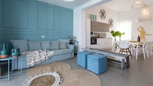 Una sala de estar moderna con una pared de acento color turquesa, un sofá, otomanas y un comedor con mesa y sillas.