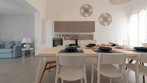 Una cocina moderna con armarios blancos, una mesa de comedor lista para cuatro personas y una sala de estar con un sofá y una lámpara.