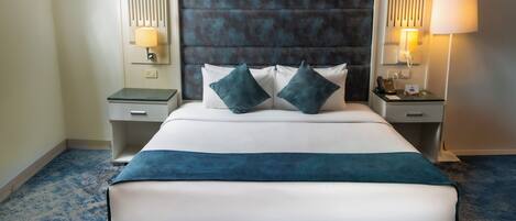 Une chambre d’hôtel avec un grand lit, deux tables de chevet, une tête de lit et un sol recouvert de moquette.