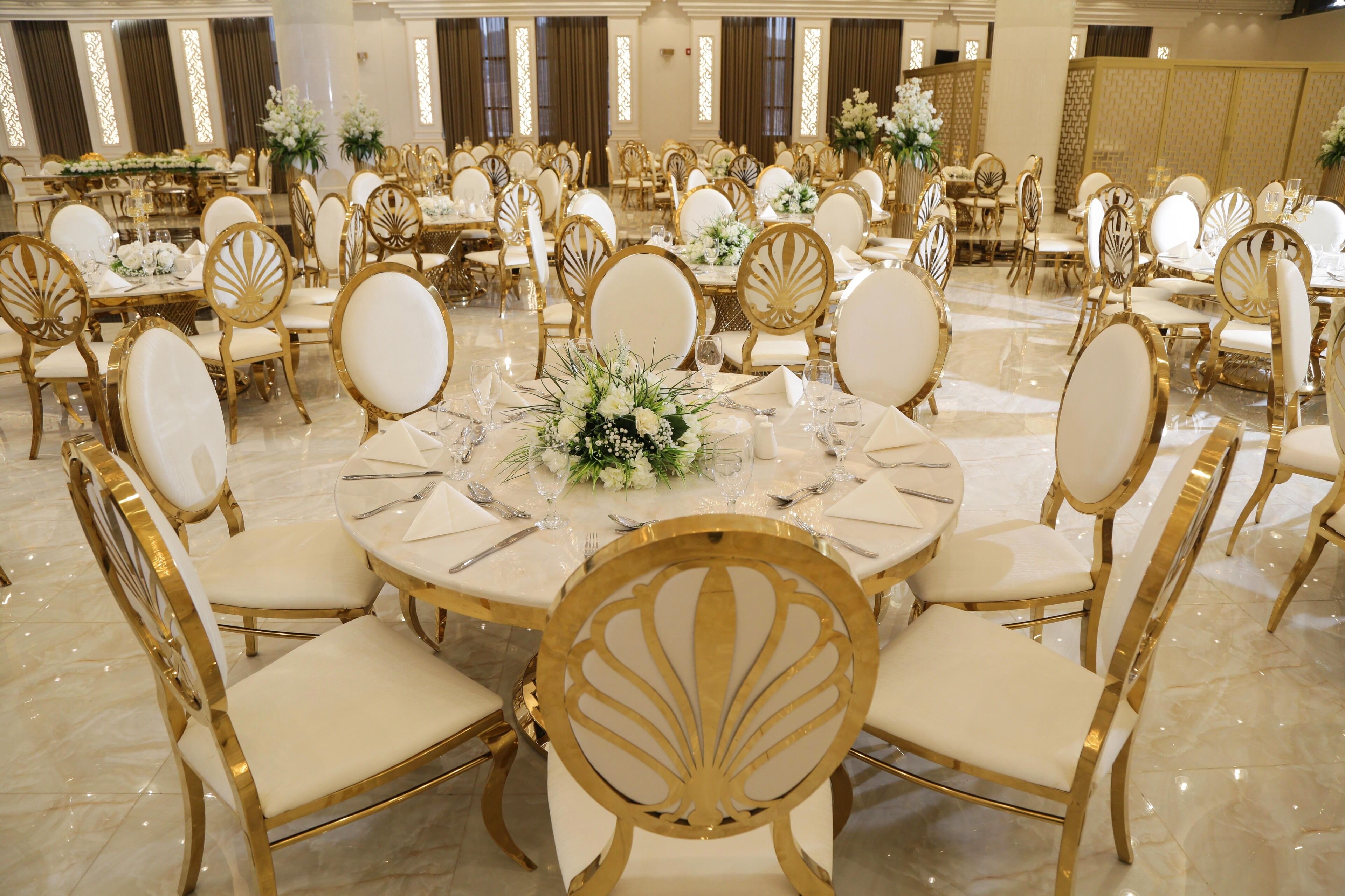 A banquet hall with round tables, gold chairs, and white tablecloths.