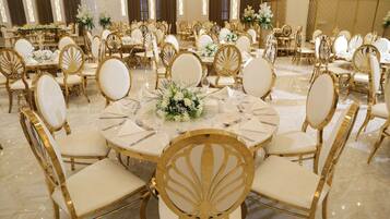 A banquet hall with round tables, gold chairs, and white tablecloths.