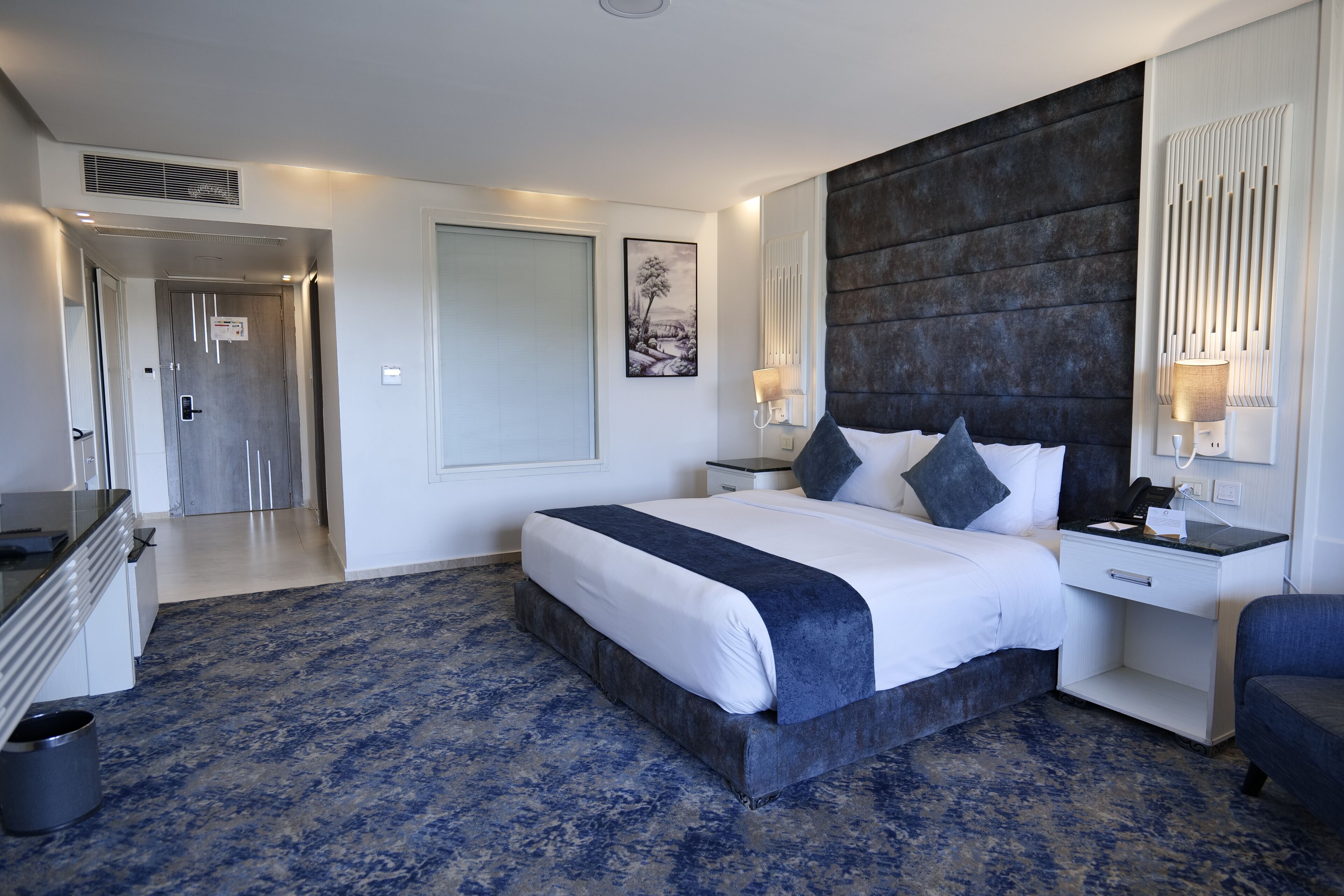 A modern hotel room with a large bed, bedside tables, a desk, and a chair.