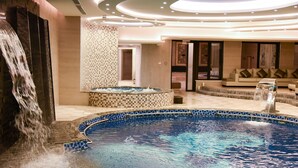 A luxurious indoor pool area with a waterfall feature, a seating area with a sofa, and a tiled wall. - Opal Hotel Amman (Amman)