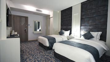 Habitación de hotel con dos camas, un espejo grande, un armario y una mesita pequeña con una tetera.