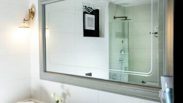 Un baño moderno con un espejo grande, un lavabo blanco y una cabina de ducha de vidrio.